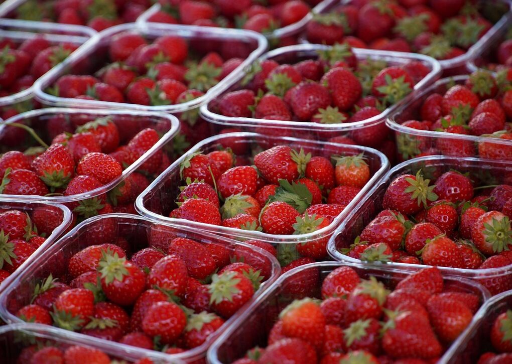 Eine Ansammlung von Erdbeeren, die in transparenten Behältern auf einem Markt oder Verkaufsstand präsentiert werden.