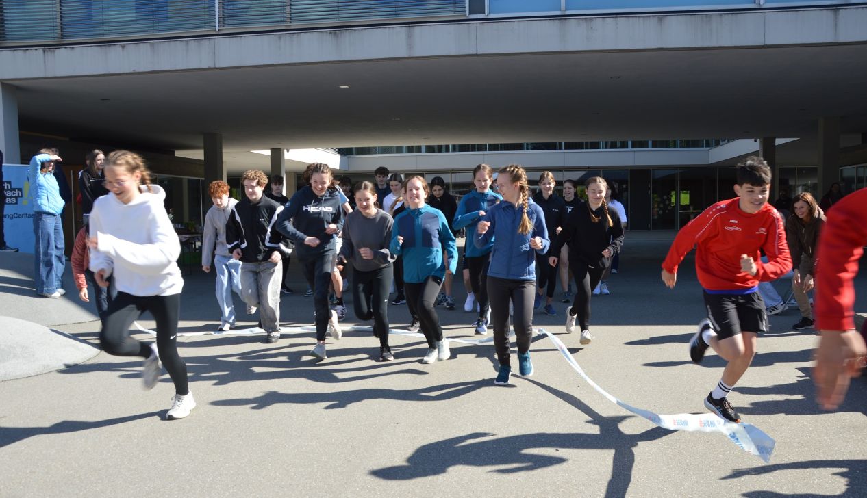 Eine Gruppe von Schülern läuft enthusiastisch im Freien. Sie tragen Sportkleidung und zeigen Freude während des Laufs.
