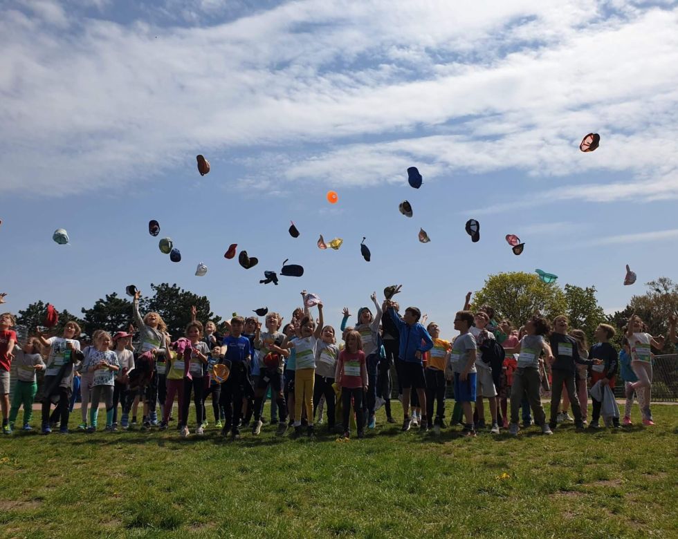 Eine Gruppe von Kindern steht auf einer Wiese und wirft ihre Hüte in die Luft, während sie sich freuen und das schöne Wetter genießen.