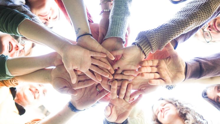 Eine Gruppe von Menschen, die ihre Hände in der Mitte zusammenlegen, symbolisieren Einheit und Zusammenarbeit.