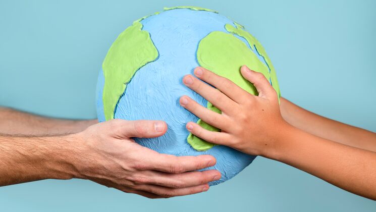 Eine Erwachsenenhands und einer Kinderhand halten gemeinsam eine Modellerde der Erde, Symbol für Zusammenarbeit und Verantwortung.