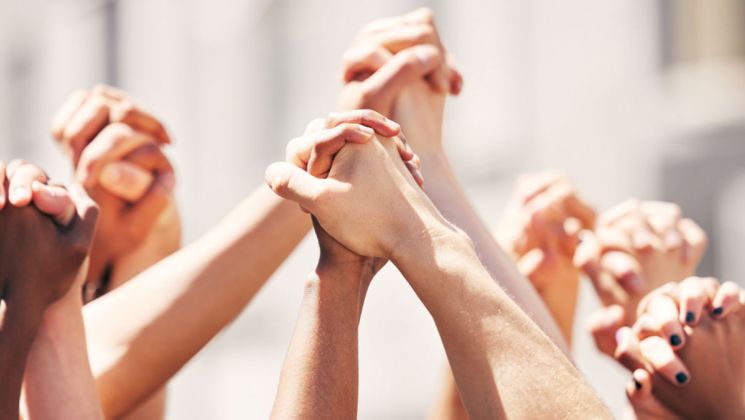Eine Gruppe von Händen unterschiedlicher Hautfarben, die sich zusammenfügen, symbolisiert Einheit und Solidarität in einem friedlichen Protest.