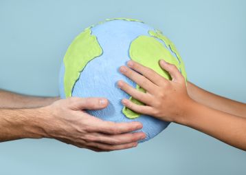 Eine Erwachsenenhands und einer Kinderhand halten gemeinsam eine Modellerde der Erde, Symbol für Zusammenarbeit und Verantwortung.