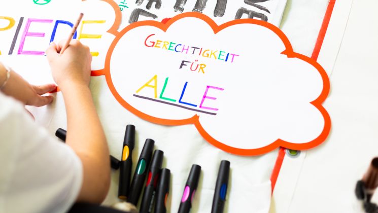 Detailaufnahme eines Papiers mit der Aufschrift 'Gerechtigkeit für Alle'. Es sind auch farbige Marker sichtbar.