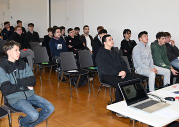 Ein Dozent spricht vor einer Gruppe von Schülern in einem Klassenzimmer. Die Teilnehmer hören aufmerksam zu und nehmen Notizen.