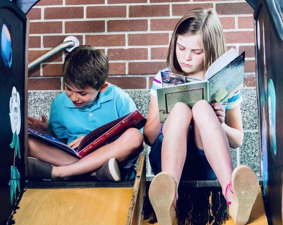 Ein Junge und ein Mädchen sitzen in einer Rutsche und lesen Bücher. Sie scheinen in ihre Geschichten vertieft zu sein.