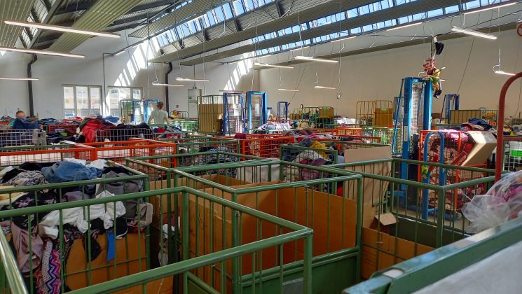 Helles, großzügiges Bekleidungsgeschäft mit Aufbewahrungskisten voller Kleidung und Kunden, die stöbern.