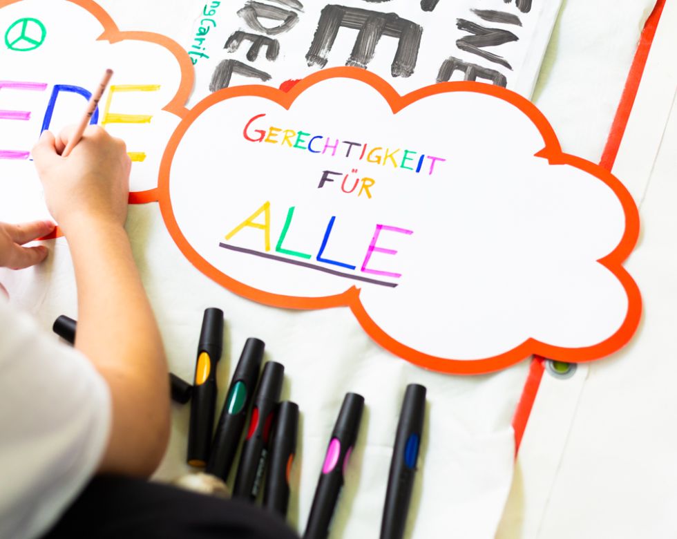 Detailaufnahme eines Papiers mit der Aufschrift 'Gerechtigkeit für Alle'. Es sind auch farbige Marker sichtbar.